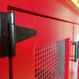 Close view of a black T-hinge on the red Farmhouse Coffee Bar Cabinet's inset door, beside the welded wire mesh panel and a bar pull