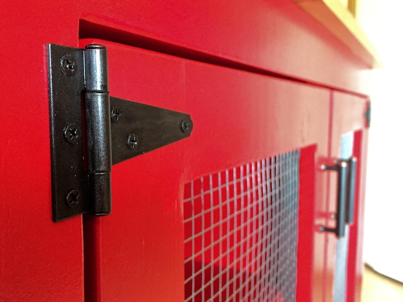Close view of a black T-hinge on the red Farmhouse Coffee Bar Cabinet's inset door, beside the welded wire mesh panel and a bar pull