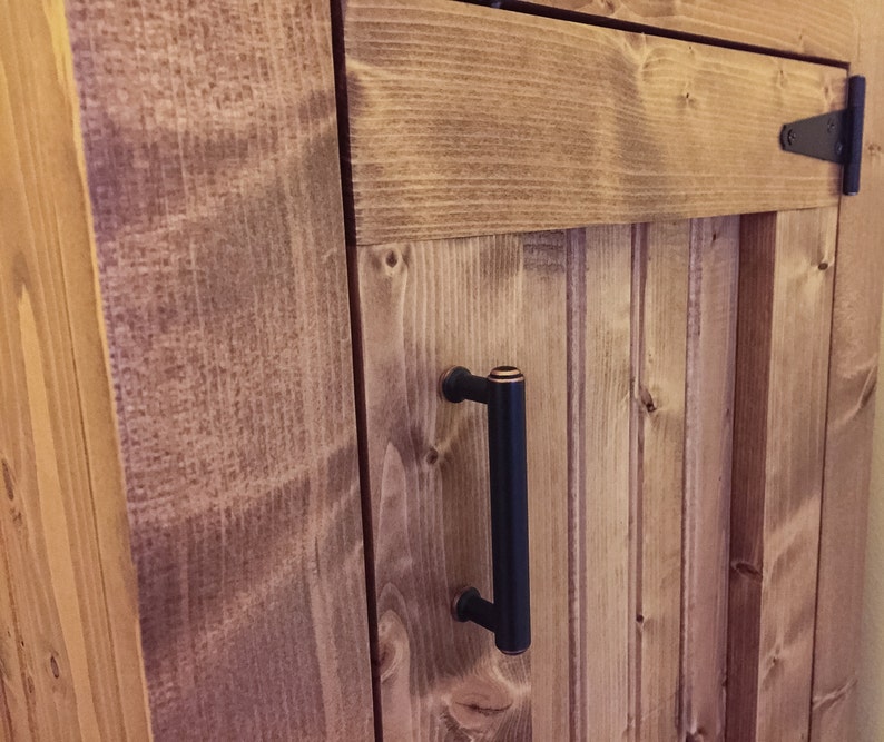 Close-up of the oil-rubbed bronze handle and T-hinge on the stained beadboard door