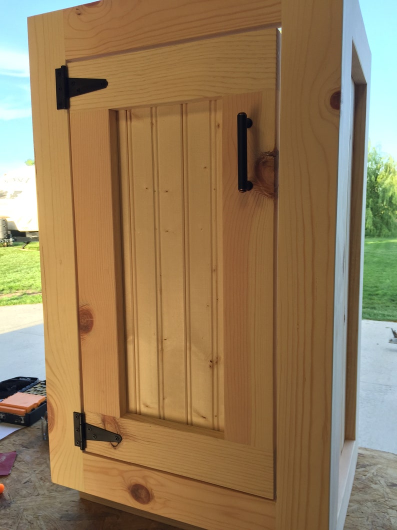 Raw unfinished pine vanity base with a beadboard door, ready for your own stain or paint