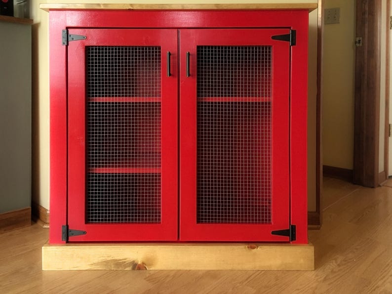 Farmhouse Coffee Bar Cabinet painted red, with welded wire mesh doors, black T-hinges, bar pulls and a stained planked pine top and base trim