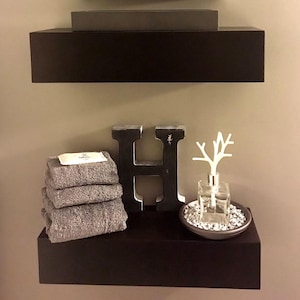 Modern black painted floating shelves with hidden wall support, displaying towels and decor in a bathroom