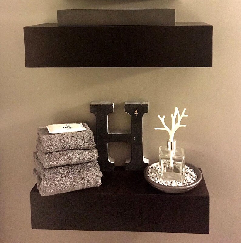 Modern black painted floating shelves with hidden wall support, displaying towels and decor in a bathroom
