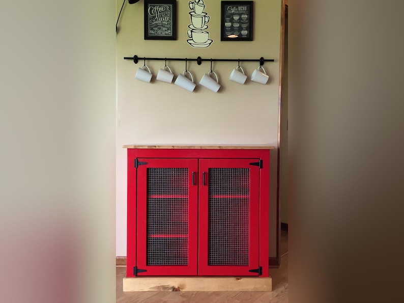 Farmhouse Coffee Bar Cabinet painted red with welded wire mesh doors, set up as a coffee station below a rail of hanging mugs and coffee prints