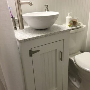 The same vanity base painted white, with satin nickel hinges and handle (on request), a granite top and a white vessel sink in a small bathroom