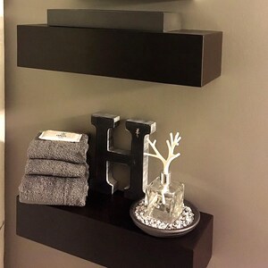 Side view of two modern black floating wall shelves in a bathroom, showing the clean painted edges
