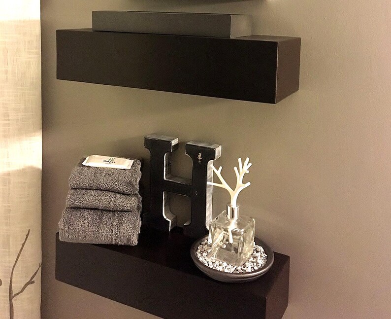 Side view of two modern black floating wall shelves in a bathroom, showing the clean painted edges
