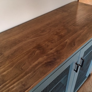 The stained wood top of the sage green Farmhouse Coffee Bar Cabinet, with its oil-rubbed bronze bar pulls and welded wire mesh doors