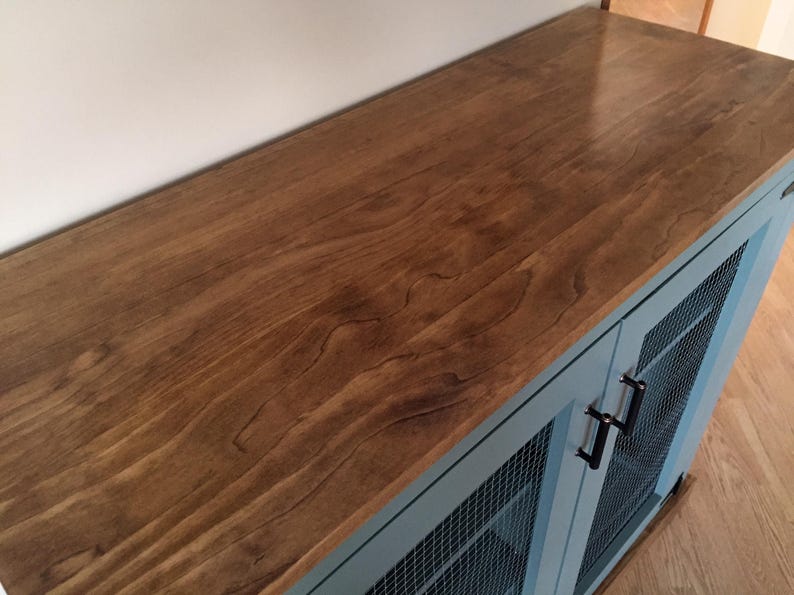 The stained wood top of the sage green Farmhouse Coffee Bar Cabinet, with its oil-rubbed bronze bar pulls and welded wire mesh doors