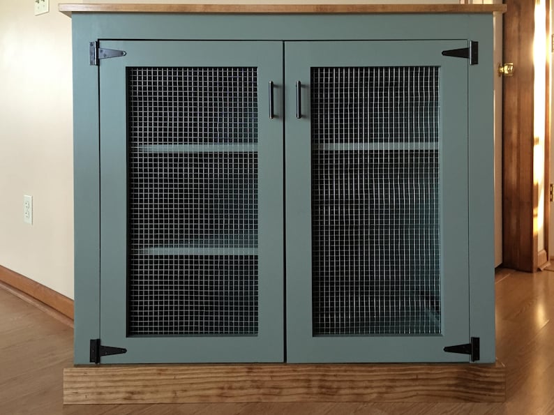 Farmhouse Coffee Bar Cabinet painted sage green, with welded wire mesh doors, black T-hinges, bar pulls and a stained top and base trim; the shelves show through the mesh