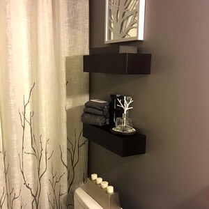 Two modern black painted floating shelves mounted over a toilet in a bathroom, minimalist wall storage