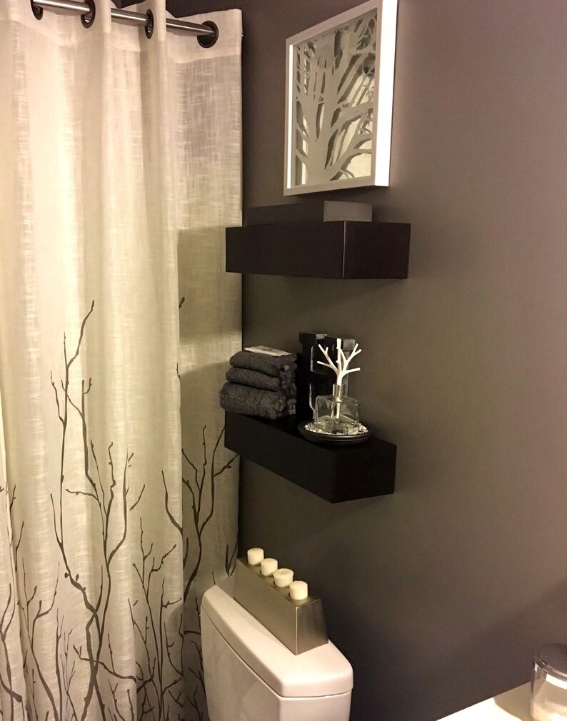 Two modern black painted floating shelves mounted over a toilet in a bathroom, minimalist wall storage