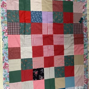 May include: A patchwork quilt with a floral border. The quilt is made of various fabrics in shades of red, green, blue, and pink. The quilt is a traditional style with a simple design.