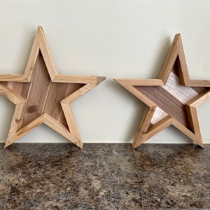 May include: Two wooden star-shaped wall decorations. The star on the left is made of light brown wood. The star on the right is made of light and dark brown wood.