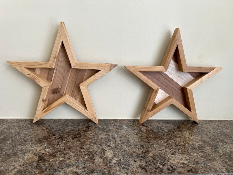 May include: Two wooden star-shaped wall decorations. The star on the left is made of light brown wood. The star on the right is made of light and dark brown wood.