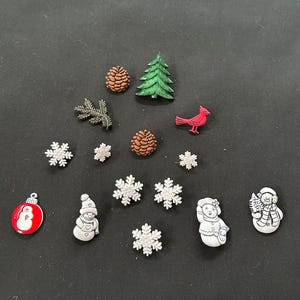 May include: A collection of Christmas-themed embellishments, including snowflakes, snowmen, a cardinal, pine cones, and a Christmas tree. The embellishments are in various colors, including red, green, white, and brown. These are ideal for crafting and holiday decorations.
