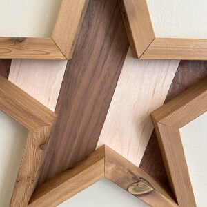 May include: A wooden star-shaped wall decoration with a geometric pattern of light and dark wood. The star is made of multiple pieces of wood that are joined together to create a unique design.