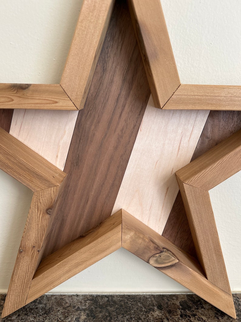 May include: A wooden star-shaped wall decoration with a geometric pattern of light and dark wood. The star is made of multiple pieces of wood that are joined together to create a unique design.