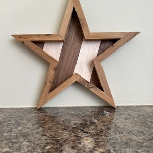 May include: A wooden star-shaped wall decoration with a geometric design. The star is made of different types of wood, including walnut and maple, and has a natural wood finish.