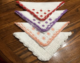 May include: Four white handkerchiefs with colourful crochet edges. The top handkerchief has a red border, the second has purple, the third has peach, and the bottom one has white.
