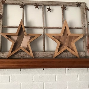 May include: Two wooden stars with a rustic finish, hanging on a window frame with a string of rusty stars. The stars are layered with different wood tones and have a farmhouse style.
