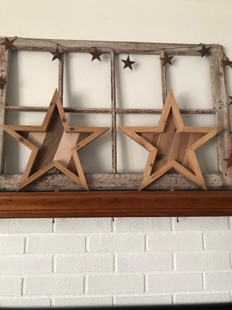 May include: Two wooden stars with a rustic finish, hanging on a window frame with a string of rusty stars. The stars are layered with different wood tones and have a farmhouse style.