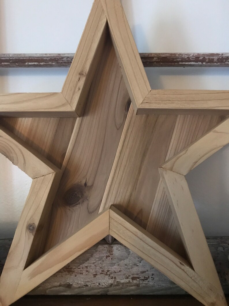 May include: A large wooden star with a rustic finish. The star is made of multiple pieces of wood that are joined together to create a three-dimensional shape.