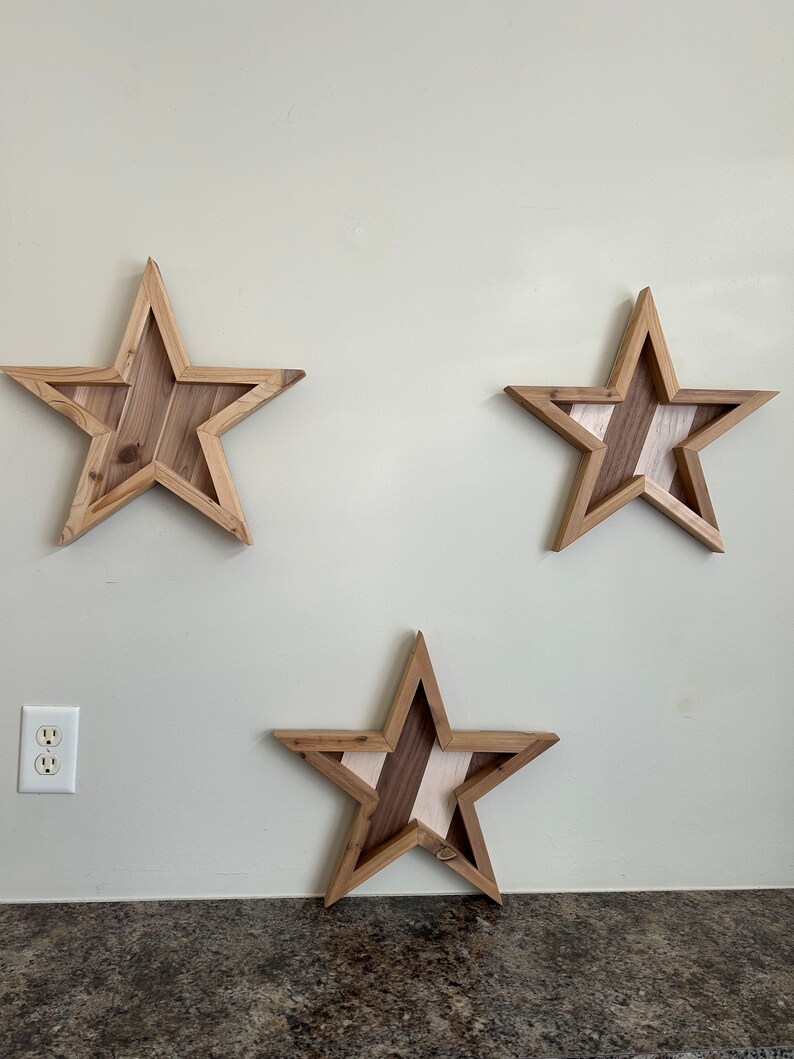 May include: Three wooden stars with a striped pattern in shades of brown and white, mounted on a light beige wall.