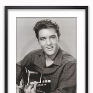 May include: Framed black and white print of a man playing a guitar. The man is smiling and wearing a plaid shirt. The print is in a black frame with a white mount.