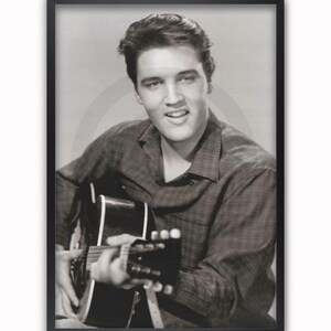 May include: Framed black and white poster of a man playing a guitar. The man is smiling and wearing a plaid shirt. The poster is in a black frame with a white background.