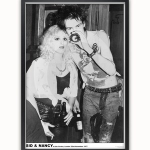 May include: Black and white photo of Sid Vicious and Nancy Spungen at the Vortex in London on November 22, 1977. Sid is holding a camera and Nancy is holding a bottle.