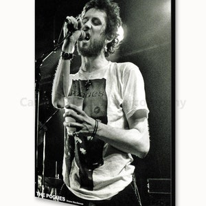 K&ouml;nnte beinhalten: Schwarz-Wei&szlig;-Poster einer Live-Musikauff&uuml;hrung. Ein Mann singt in ein Mikrofon und h&auml;lt ein Glas. Er tr&auml;gt ein T-Shirt mit dem Aufdruck "The Pogues". Das Poster enth&auml;lt den Namen der Band und den Namen von Shane MacGowan.