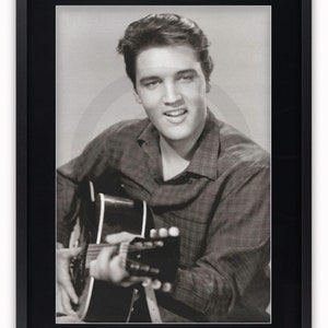 May include: Framed monochrome print of a man playing a guitar and smiling. The man wears a checked shirt. The print is in a black frame. The text at the bottom says "The Copyright logo will be removed from your poster."