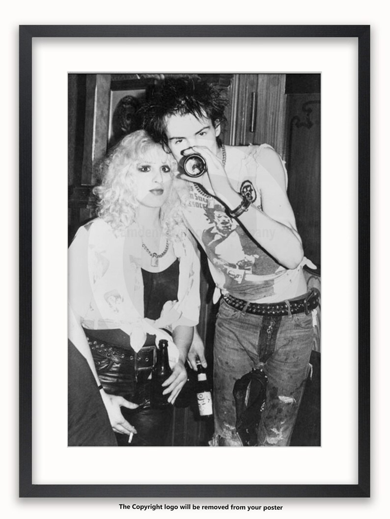 May include: A black and white photo of a man and a woman. The man is wearing a sleeveless shirt with a graphic on it and the woman is wearing a white shirt with a necklace. The man is holding a camera up to his eye and the woman is holding a cigarette in her hand.
