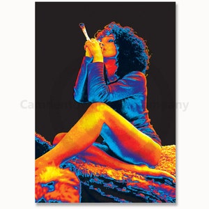 May include: A woman with dark hair sits on a rug, wearing a blue shirt and holding a lit joint in her hand. The image is in a thermal colour scheme, with reds, oranges, and blues.