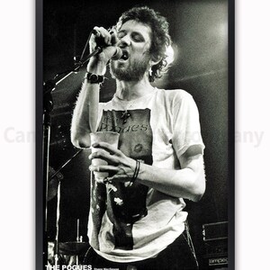 K&ouml;nnte beinhalten: Schwarz-Wei&szlig;-Poster mit einem Live-Auftritt von The Pogues. S&auml;nger Shane MacGowan singt in ein Mikrofon und h&auml;lt einen Becher. Der Name der Band und des S&auml;ngers sind am unteren Rand des Posters aufgedruckt.