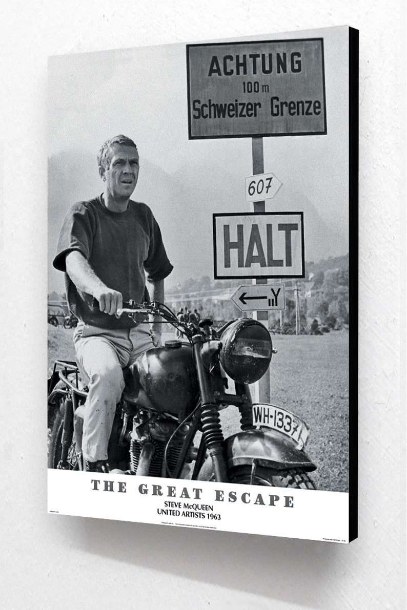 May include: Black and white poster featuring Steve McQueen on a motorcycle. The image includes signs with German text, including "ACHTUNG" and "Schweizer Grenze." The poster also displays the film title "THE GREAT ESCAPE."