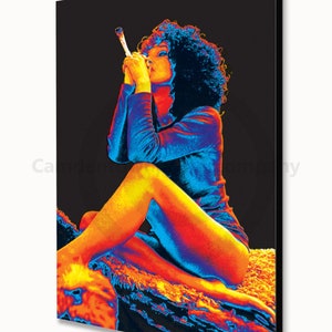 May include: A woman with curly hair sits on a textured surface, wearing a blue and orange outfit. She is holding a long, thin object to her lips.