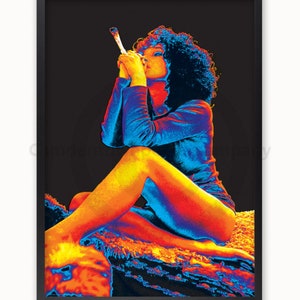 May include: A woman with curly hair sits on a rock, wearing a blue and orange shirt. She is holding a white object in her hand and looking down.