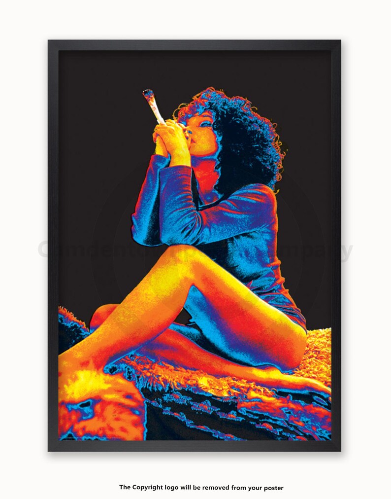 May include: A woman with curly hair sits on a rock, wearing a blue and orange shirt. She is holding a white object in her hand and looking down.