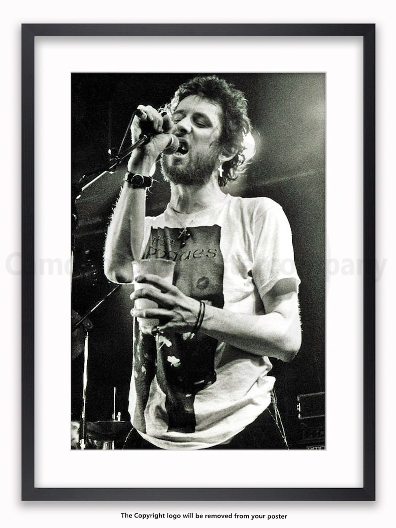 K&ouml;nnte beinhalten: Schwarz-wei&szlig; gerahmtes Poster einer Live-Musik-Performance. Eine Person singt in ein Mikrofon, h&auml;lt einen Becher und tr&auml;gt ein T-Shirt mit dem Aufdruck "Pogues". Das Bild ist eine Nahaufnahme des Darstellers auf der B&uuml;hne.