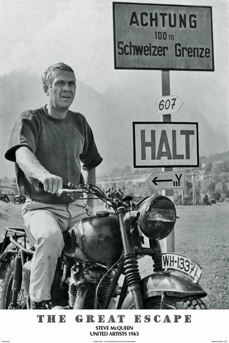 May include: Black and white image of Steve McQueen on a vintage motorcycle. The motorcycle has a headlight, a license plate, and a dark fuel tank. Signs in German read "Achtung" and "Schweizer Grenze". The film title "The Great Escape" is at the bottom.