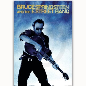 May include: A black and white poster featuring Bruce Springsteen and the E Street Band. The poster has a blue background with a faded effect. Bruce Springsteen is playing a guitar and is wearing a black shirt and jeans. The text "Bruce Springsteen and the E Street Band" is in gold lettering.