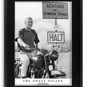 May include: Black and white framed poster featuring Steve McQueen on a motorcycle from "The Great Escape." The poster includes the film title, credits, and German signage reading "Achtung" and "Schweizer Grenze."