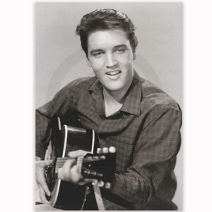 May include: A monochrome portrait of a man playing a guitar. The man is smiling and wearing a plaid shirt. The guitar is black and white. The image is a vintage photograph.