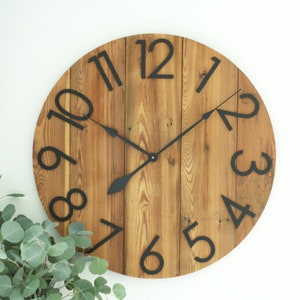 May include: A large, round wooden clock with black Roman numeral hour markers and black hands. The clock face is made of reclaimed wood planks.