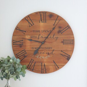 May include: A wooden clock with Roman numeral markings and the text "Time spent with family is worth every second" with a small leafy design below. The clock has black hands and a brown wood background.