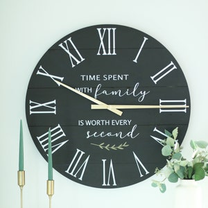 May include: Black wooden clock with white Roman numeral markings and gold hands. The clock face has the text "Time spent with family is worth every second" with a small green leaf design.