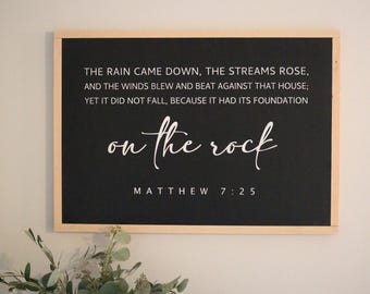 May include: Black framed sign with white text that reads "THE RAIN CAME DOWN, THE STREAMS ROSE, AND THE WINDS BLEW AND BEAT AGAINST THAT HOUSE; YET IT DID NOT FALL, BECAUSE IT HAD ITS FOUNDATION on the rock MATTHEW 7:25"