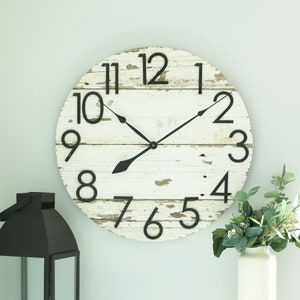May include: A white farmhouse-style clock with black Roman numeral hour markers and black hands. The clock face has a distressed woodgrain texture.